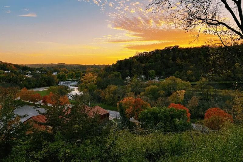 Autumn sunset view from Church Hill Overlook in Lanesboro, Minnesota, showing the Root River Valley with vibrant fall foliage, rolling bluffs, and the river winding through town below.