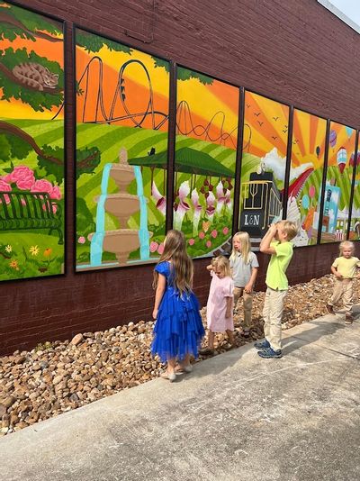 Children look for the five cats hidden in the Foley Main Street community mural in Downtown Foley