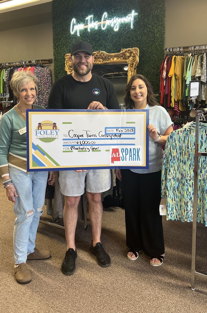 Cooper Twins Consignment Shop is a 2025 Winner of a $1,000 marketing grant through ALSPARK.. Accepting the check is owner BL Cooper. Foley Main Street board members Deborah Mixon and Sabrina May presented the check.