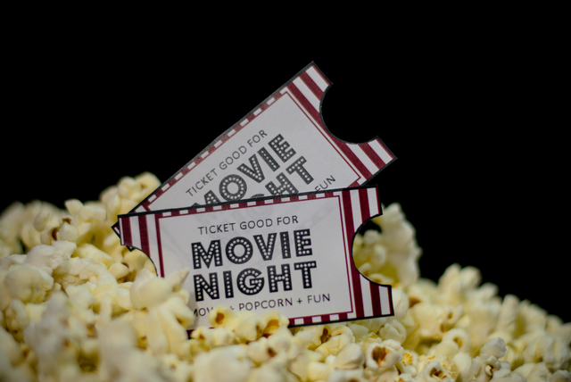 Close-up of two red-and-white movie tickets partially tucked into a pile of fresh popcorn against a dark background. The tickets read “Movie Night” and suggest a fun, classic cinema experience.