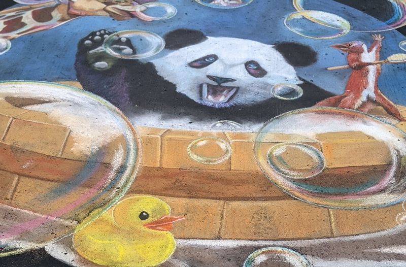 A chalk pastel drawing of a panda having a bubble bath, a squirrel trying to catch bubbles on a wood spoon, and a yellow rubber duck sitting next to the tub in a puddle.