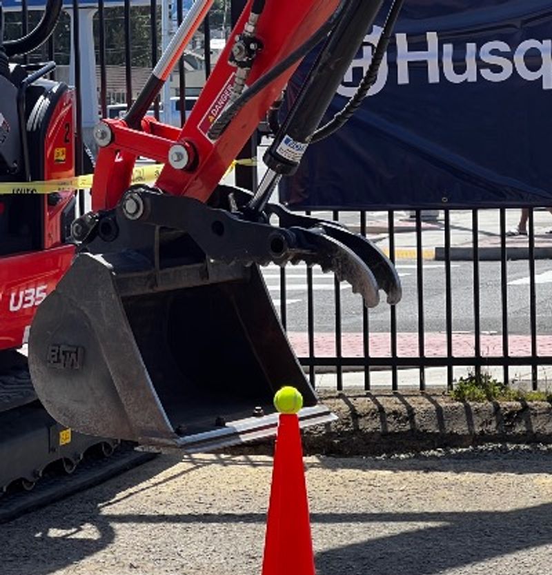 A contestant attempts to pick up a tennis ball from a cone with an earth mover