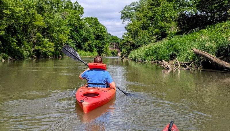 A POV-style photo of kayaking the Root River near Lanesboro, MN with a person visible in a kayak wearing a life jacket