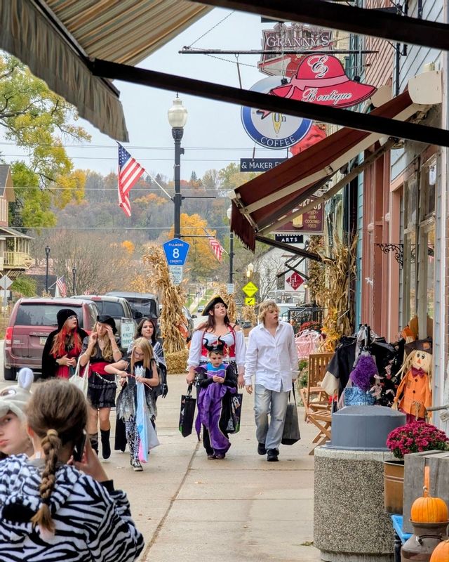 Families and children in Halloween costumes walk along decorated storefronts in downtown Lanesboro, Minnesota, during a fall trick-or-treating event.