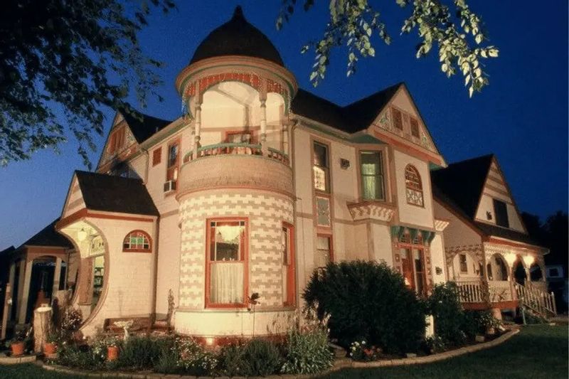The historic Scalan House in Lanesboro illuminated at dusk, showcasing its ornate Victorian architecture, turret, and decorative trim surrounded by trees.