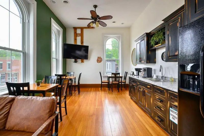 Bright lounge and kitchenette at the Iron Horse Inn Phoenix space, featuring tall arched windows, hardwood floors, café tables, and a modern coffee station in downtown Lanesboro.