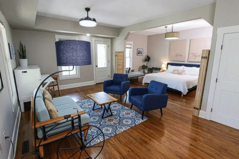 The Bluff Country Suite at the Root River Inn features a spacious open layout with a sitting area, blue accent chairs, wood floors, and a comfortable bed, offering a modern and relaxing retreat for guests in Lanesboro.