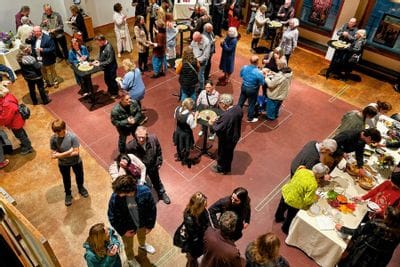 Overhead view of a lively reception in the Commonweal Theatre lobby, with guests mingling around cocktail tables and buffet tables during an opening night gathering in Lanesboro.