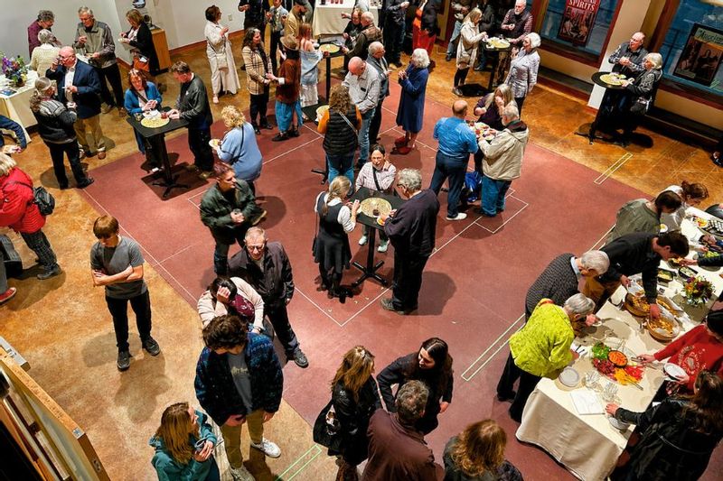 Overhead view of a lively reception in the Commonweal Theatre lobby, with guests mingling around cocktail tables and buffet tables during an opening night gathering in Lanesboro.