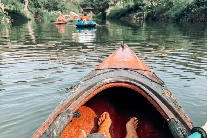 A view from inside a kayak floating down the Root River with other paddlers ahead, capturing a relaxed river trip with Root River Outfitters surrounded by lush riverbanks.