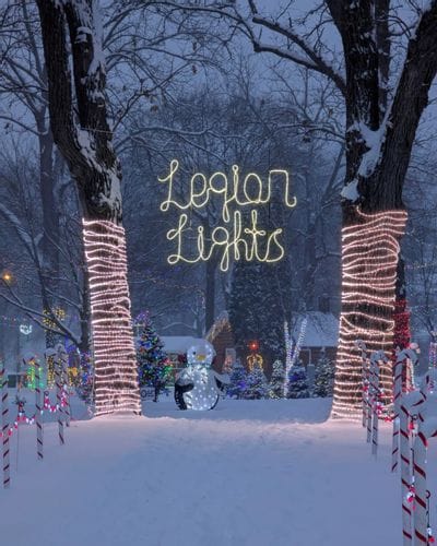 Snow-covered trees and colorful holiday displays glow beneath a “Legion Lights” sign at the Lanesboro Legion Lights display in Lanesboro, Minnesota.