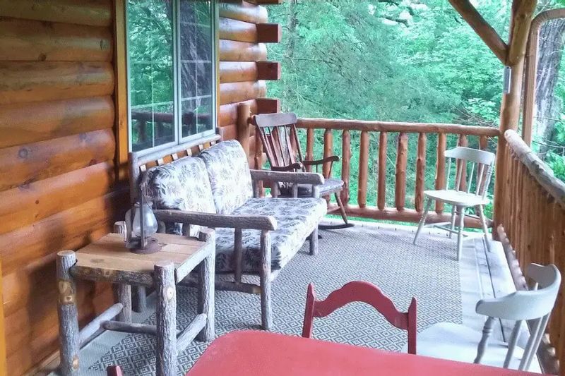 Covered deck at a log cabin overlooking the Root River Valley, with rustic chairs, a wooden bench, and forest views creating a peaceful outdoor seating area.
