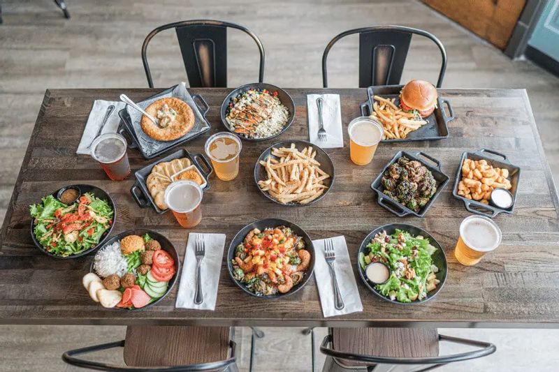 An overhead view of a table at Pedal Pushers Café filled with burgers, fries, salads, appetizers, and craft beers, showcasing a variety of casual dining options in downtown Lanesboro.