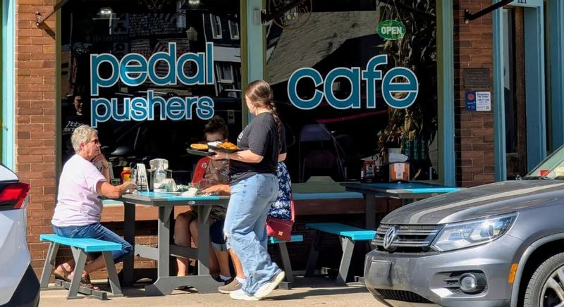 People enjoy outdoor seating at Pedal Pushers Café in downtown Lanesboro, with a server delivering food to a sidewalk table outside the café’s large front windows.