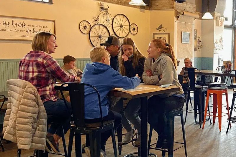 A family sits together at a table inside a casual café, talking and sharing a meal in a warm, welcoming dining space popular with locals and visitors.