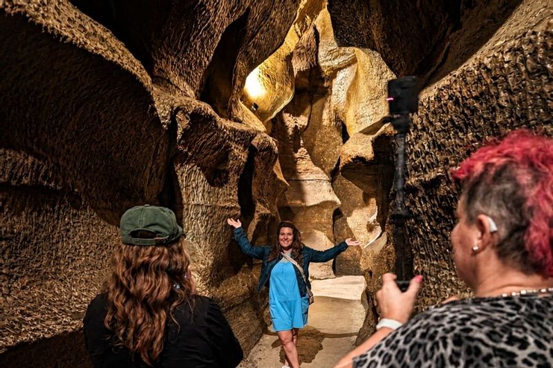 Visitors take photos inside Niagara Cave near Harmony, Minnesota, where a woman poses in a narrow limestone passage surrounded by dramatic cave walls and warm lighting.
