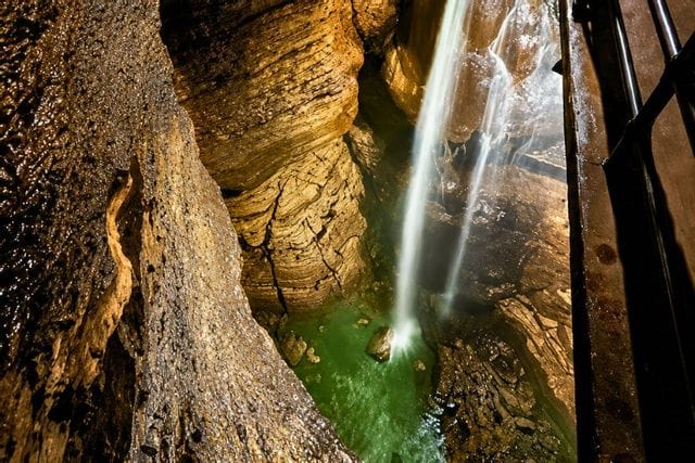 Water cascades down a rocky cave wall inside Niagara Cave, highlighting textured stone surfaces and flowing water illuminated in warm tones.