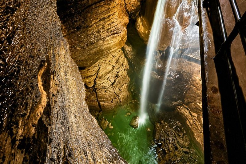 Water cascades down a rocky cave wall inside Niagara Cave, highlighting textured stone surfaces and flowing water illuminated in warm tones.