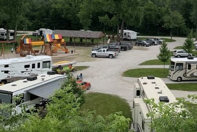 RVs and vehicles are parked throughout Eagle Cliff Campground, with a colorful playground, picnic shelter, and wooded surroundings visible in this family-friendly camping area near Lanesboro, Minnesota.