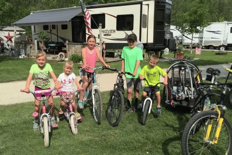 A group of children stand with their bicycles on a grassy campsite at Eagle Cliff Campground, with RVs and bike trailers in the background, ready for a family-friendly biking adventure near Lanesboro, Minnesota.