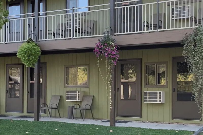 A row of ground-level motel rooms with patio chairs, hanging flower baskets, and balconies above sits amid green lawn at Eagle Cliff Campground near Lanesboro, Minnesota.