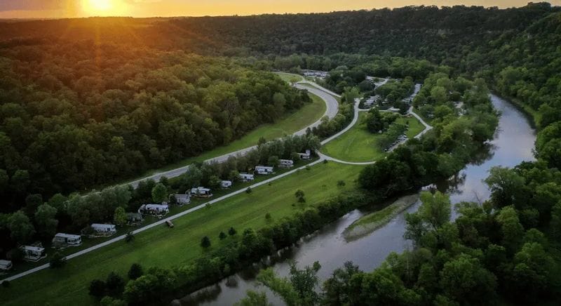 An aerial view of Eagle Cliff Campground at sunset, showing winding roads, campsites, wooded bluffs, and the Root River flowing through the green valley near Lanesboro, Minnesota.