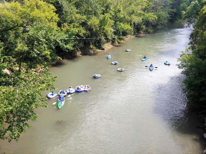 Kayakers and tubers floating down the Root River near Lanesboro, Minnesota, surrounded by wooded riverbanks