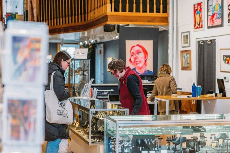 Visitors browse jewelry and artwork inside Lanesboro Arts Gallery, with local art displays and a portrait painting visible in the background.