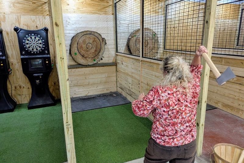 Person throwing an axe toward a wooden target inside an indoor axe-throwing lane at Raging Root Adventure Arcade in Lanesboro, Minnesota.