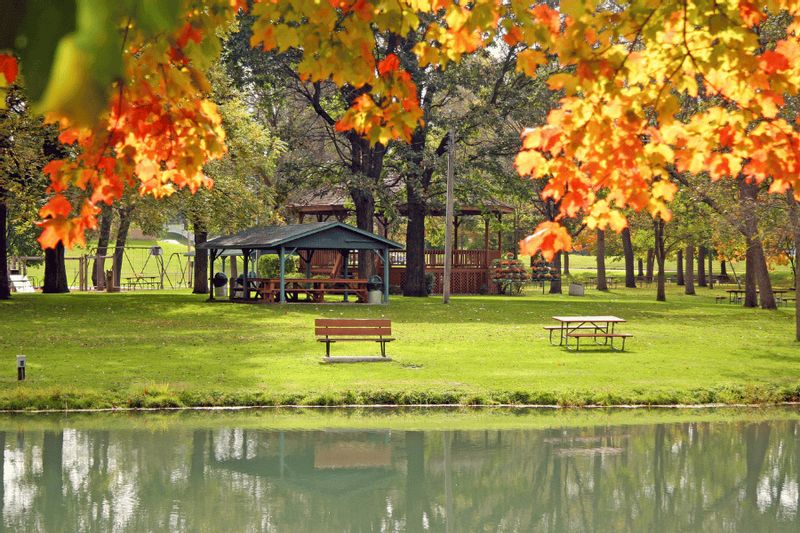 Fall foliage frames Sylvan Park in Lanesboro, Minnesota, with picnic tables, a pavilion, and trees reflected in a calm pond.