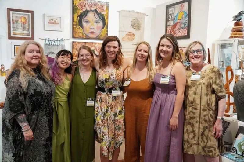 Lanesboro Arts staff members and local artists stand together inside a gallery, smiling in front of colorful artwork displayed on the walls.