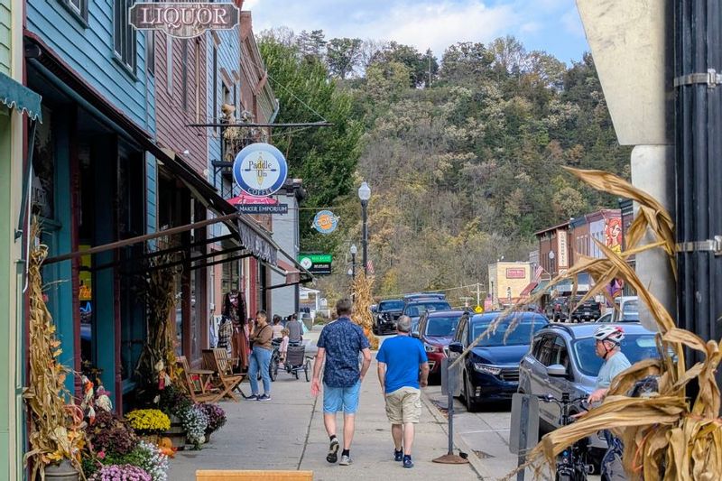Visitors stroll along downtown Lanesboro, Minnesota, on a fall day, with seasonal decorations, local shops, and wooded bluffs in the background.