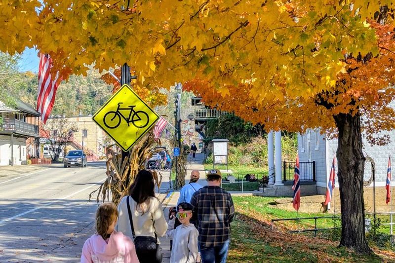 Visitors stroll along downtown Lanesboro, Minnesota, on a fall day, with seasonal decorations, local shops, and wooded bluffs in the background.