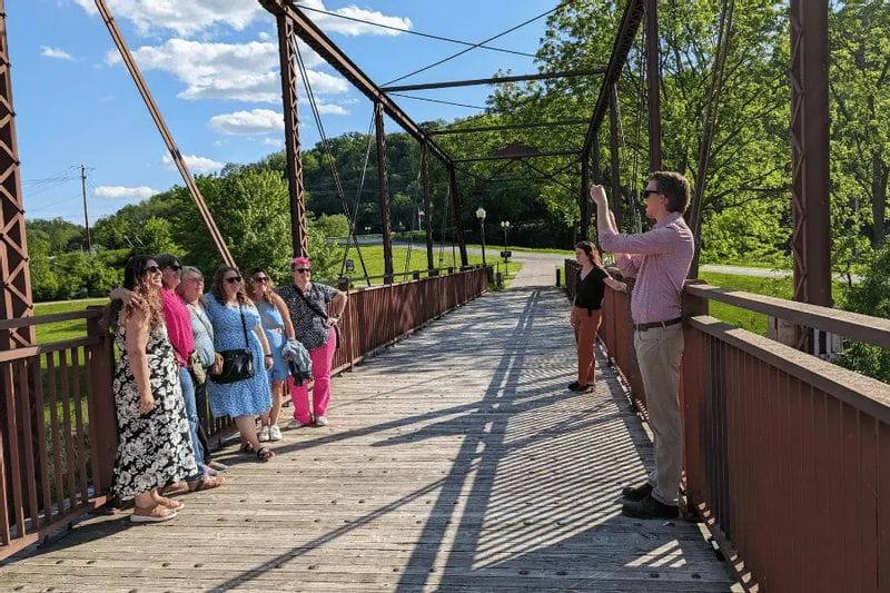 Visitors pose for a group photo on a historic iron bridge in Lanesboro, Minnesota, surrounded by green trees.
