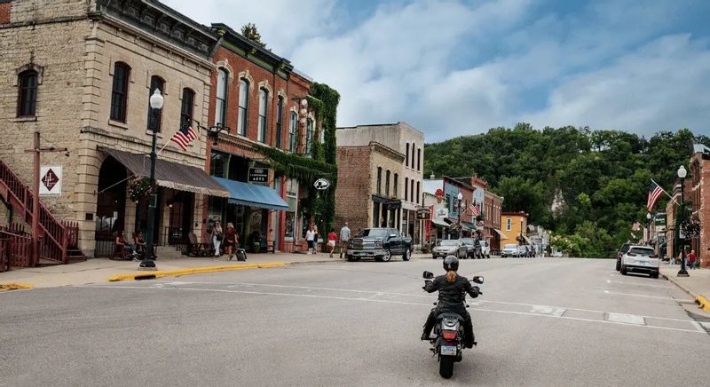Motorcyclist riding through historic downtown Lanesboro, Minnesota, lined with brick storefronts and local shops.