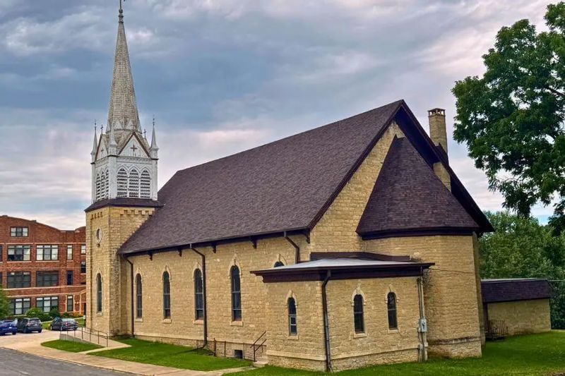 A historic stone church in Minnesota with a steeply pitched roof and tall steeple, shown after a roof renovation project completed by Minnesota Building Contractors.
