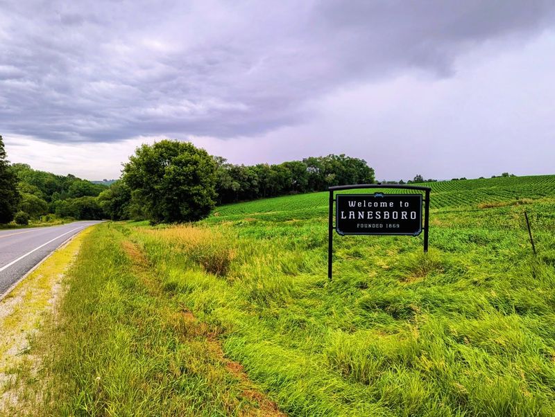 Welcome to Lanesboro sign along County Road 8, surrounded by rolling green fields and trees, marking the entrance to Lanesboro, Minnesota in the Root River Valley