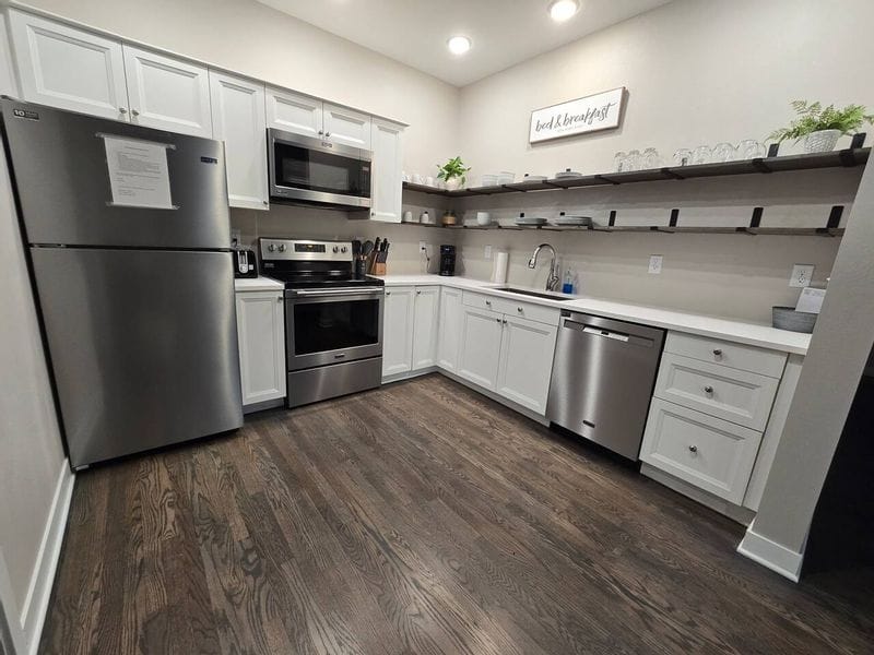 Shared guest kitchen at Parkway Place AirBnB in Lanesboro, featuring white cabinetry, stainless steel appliances, open shelving, and a clean, modern design with wood flooring.