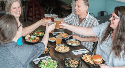 A group of friends raise glasses of craft beer in a toast around a table filled with burgers, fries, and salads at a casual restaurant in Lanesboro.