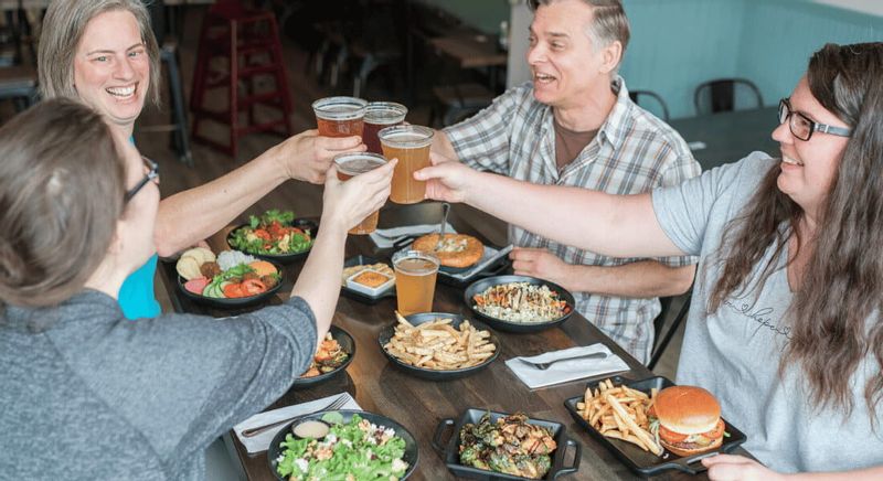 A group of friends raise glasses of craft beer in a toast around a table filled with burgers, fries, and salads at a casual restaurant in Lanesboro.