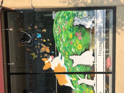 A window painting of a small dog chasing butterflies on a grass hill covered with wild flowers.