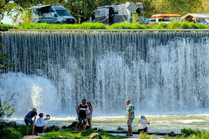 People and a dog posing for photos in front of the Lanesboro Dam