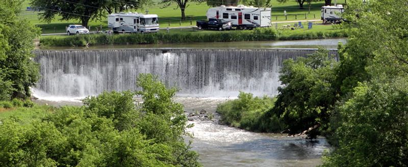 Aerial view of the Lanesboro Stone Dam surrounded by lush greenery with RVs parked at the campground above
