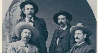 Black-and-white historical portrait of four late-19th-century men wearing wide-brimmed hats and suits, posed together with mustaches and period clothing against a studio backdrop.