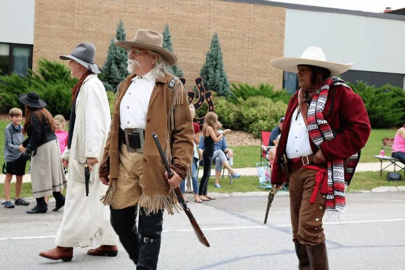 Actors dressed in period frontier clothing portray Buffalo Bill–era figures during a community event, walking along a street in Lanesboro with spectators watching in the background.