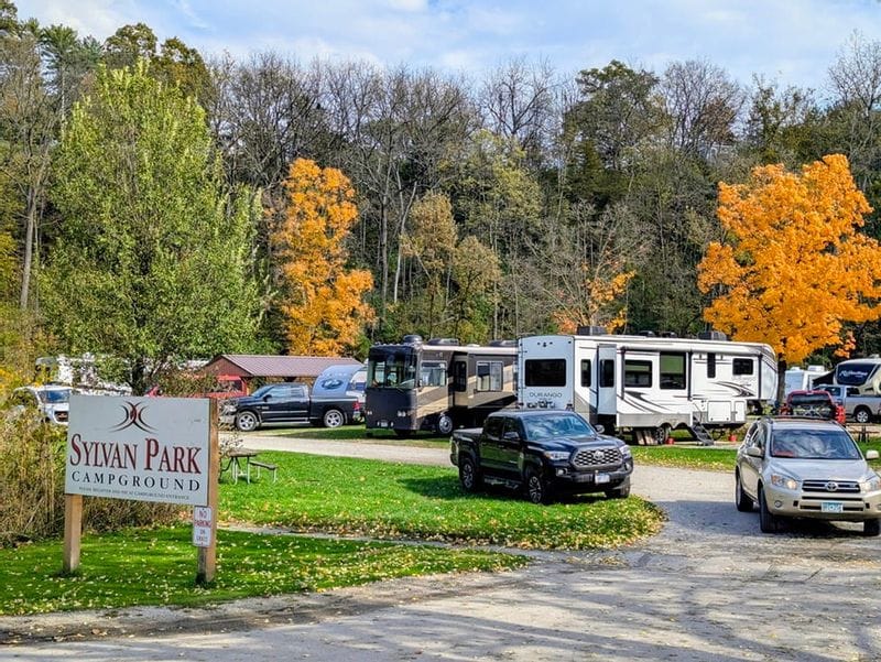 RVs and vehicles parked at Sylvan Park Campground in Lanesboro, Minnesota, surrounded by fall foliage and trees in autumn color.