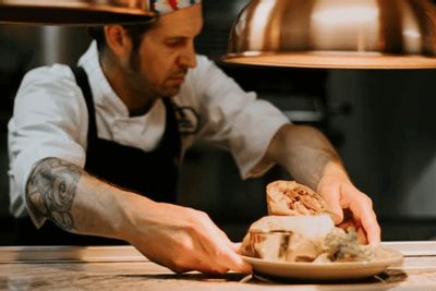 A chef plates a freshly prepared dish in a restaurant kitchen, carefully arranging food under warm lights, highlighting the craft and care behind a locally made meal.
