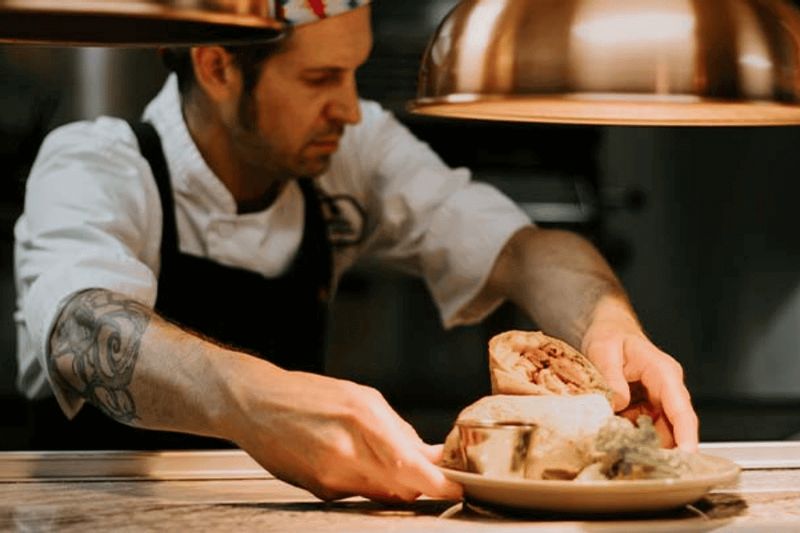 A chef plates a freshly prepared dish in a restaurant kitchen, carefully arranging food under warm lights, highlighting the craft and care behind a locally made meal.