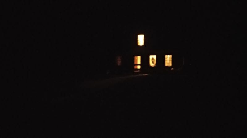 A dark night with a home in the distance with some of the windows alight.