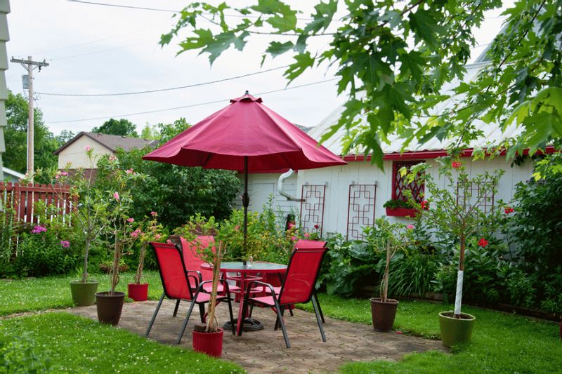 Outdoor garden patio at A Guest Hus with a red umbrella, matching table and chairs, potted plants, and lush greenery surrounding a cozy seating area.